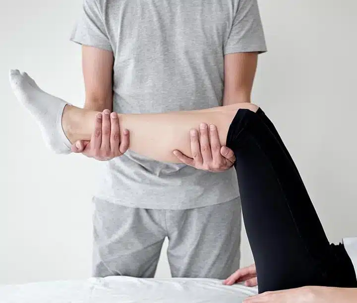 Terapeuta wykonuje precyzyjne rozciąganie łydki pacjenta, wspomagające regenerację mięśni i zwiększenie ruchomości